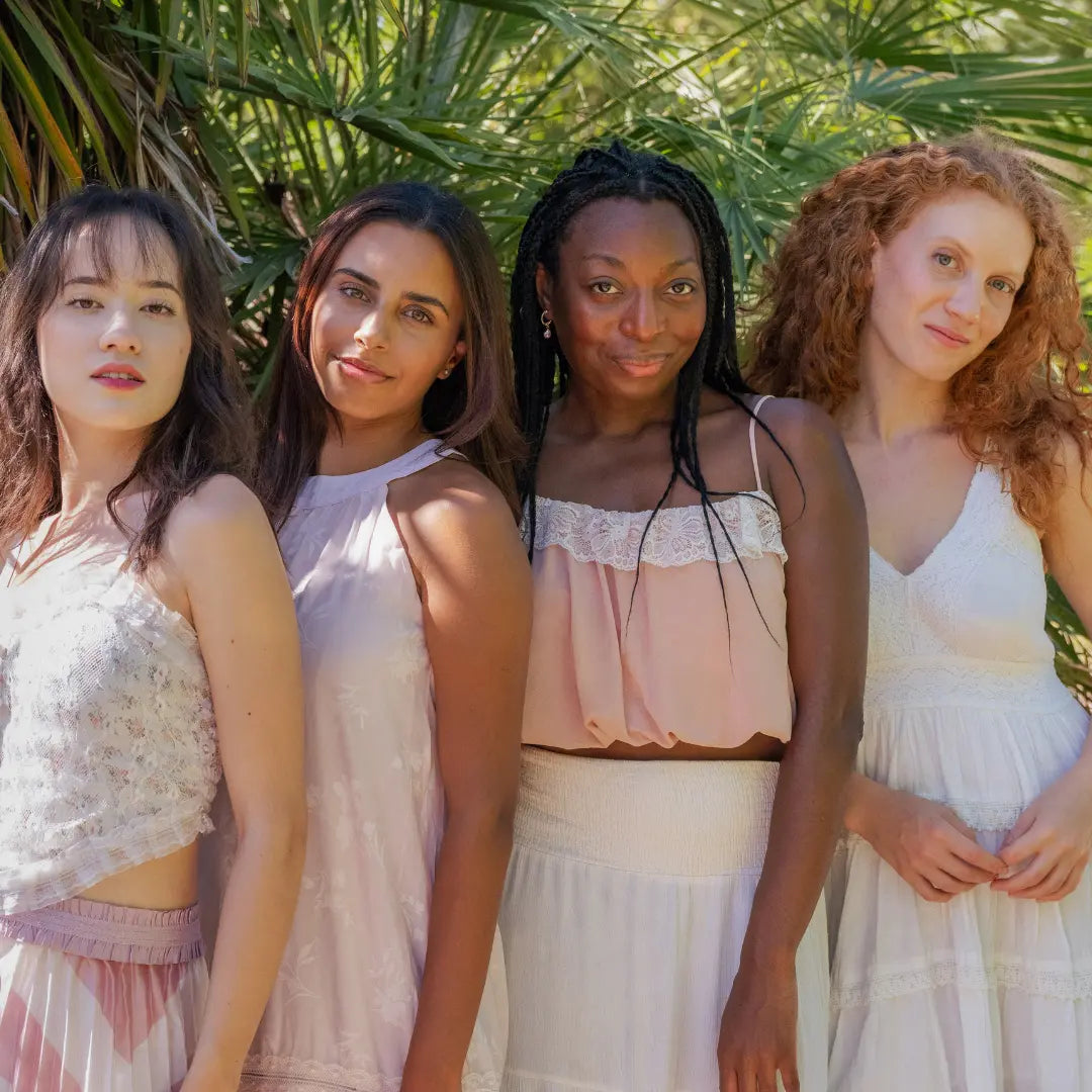4 jolies femmes en robes blanche et rose poudré. Un femme asiatique, une femme indienne, une femme noire et une femme blanche.