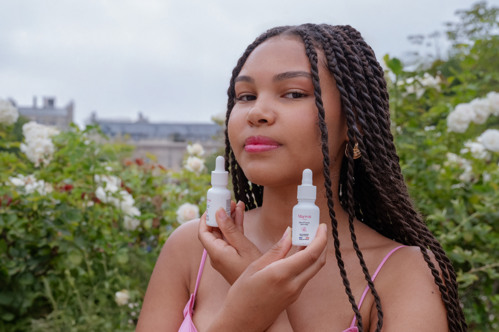 Jolie femme métisse avec de longues tresses. Elle tient dans ses deux mains 2 flacons de sérums Élixir D'amour de Mawu Paris.