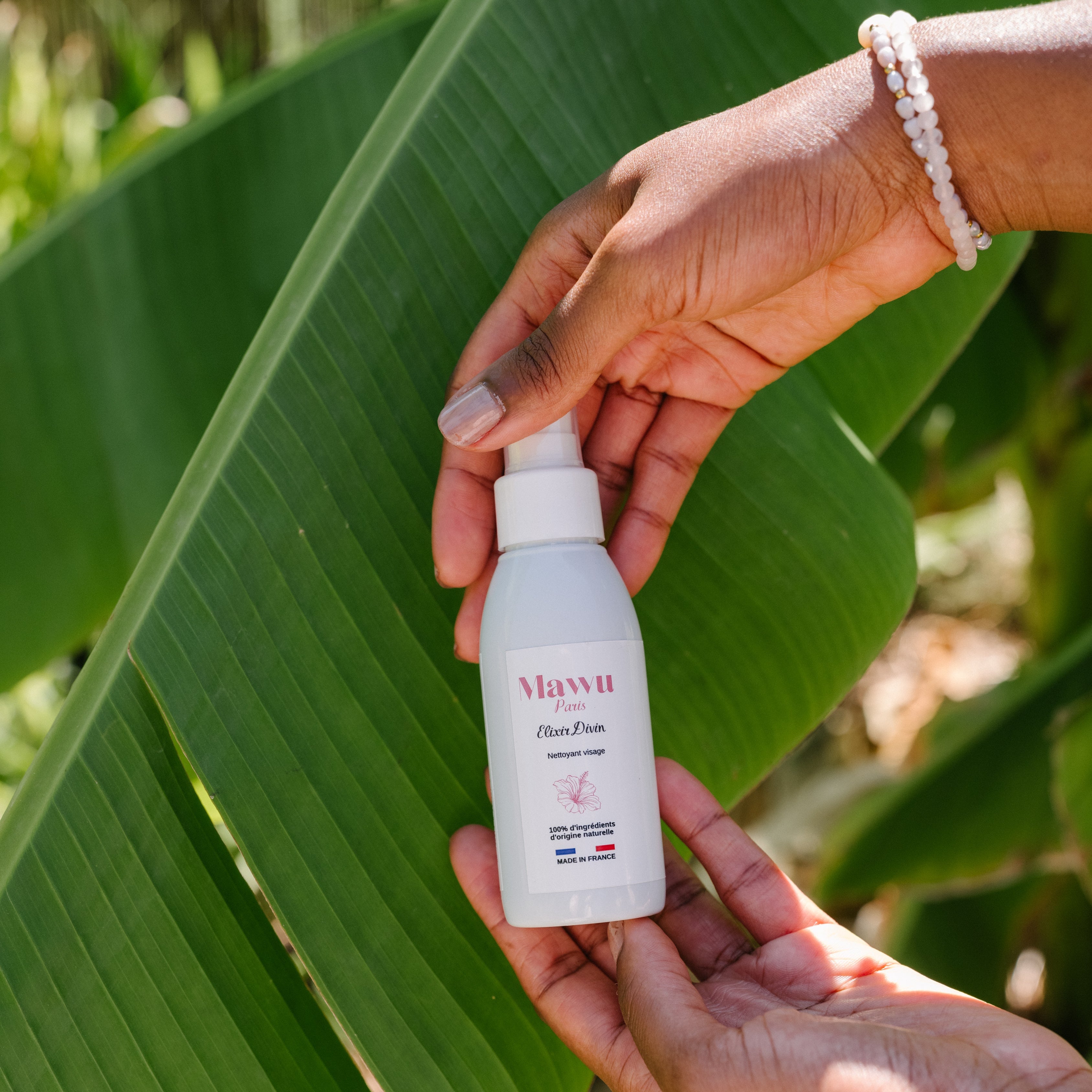 Des jolies mains de femme noire avec 2 bracelets en perles au poigné droit, tiennent l'huile nettoyant Élixir Divin de Mawu Paris.