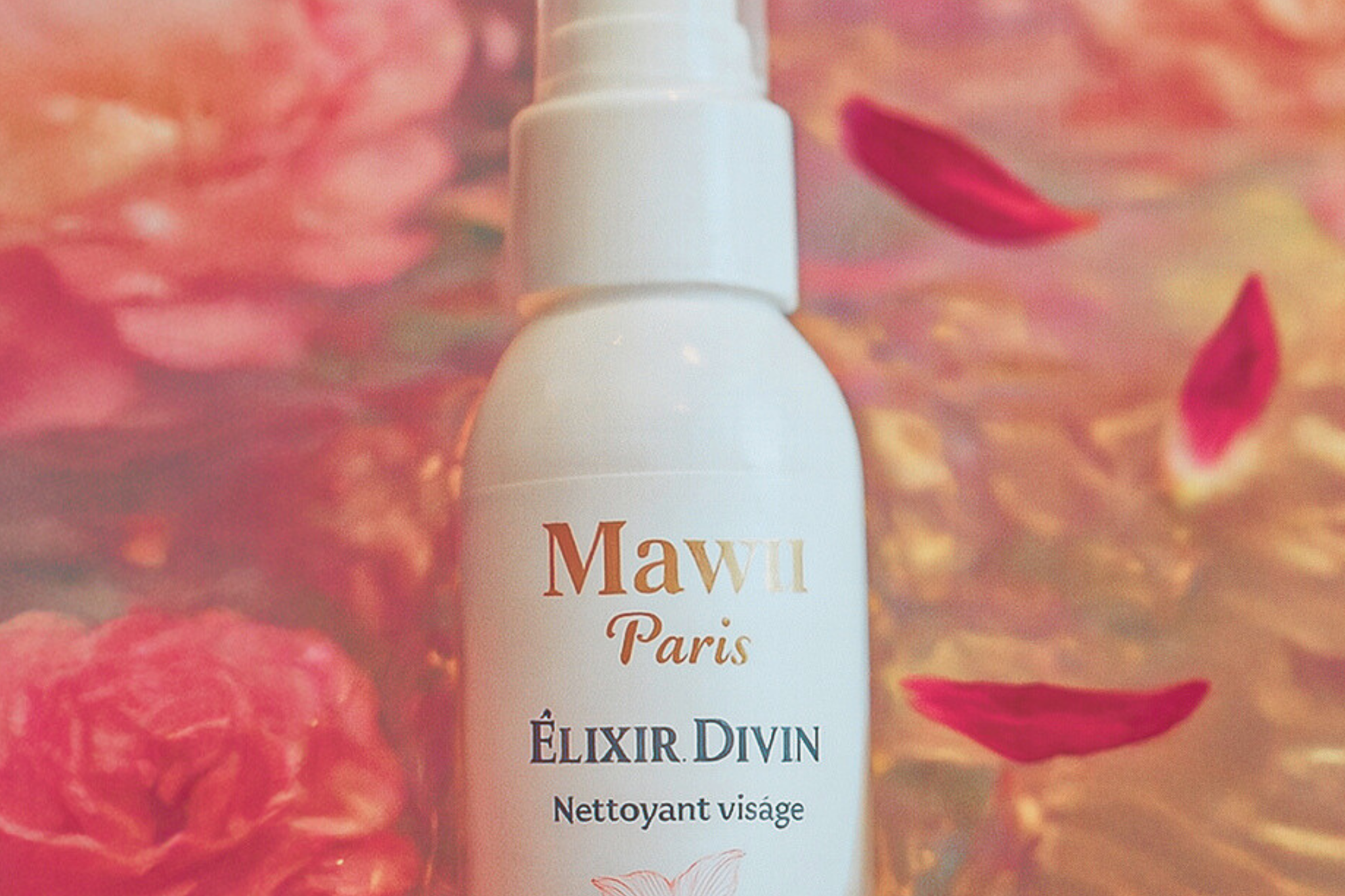Un flacon d'huile nettoyante Élixir Divin de Mawu Paris, à la surface de l'eau avec des roses et des pétales de fleur d'hibiscus.