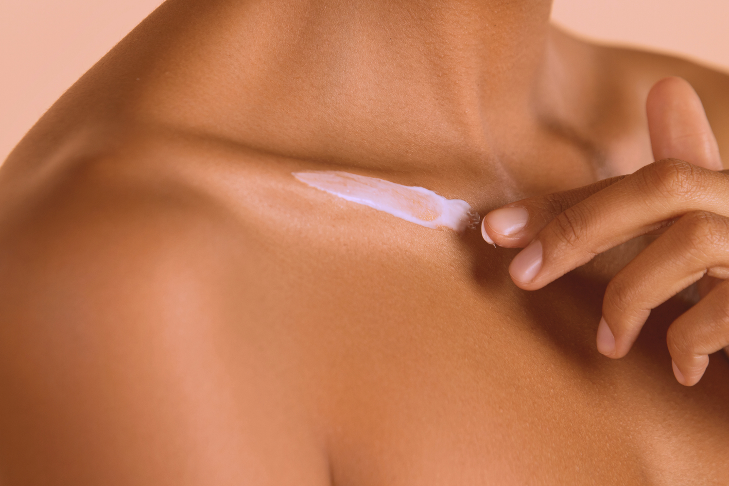 Une goutte de crème étalée sur la clavicule d'une femme à la peau noire.