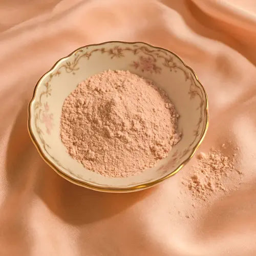 Argile rose en poudre, dans un bol en porcelaine à bord doré posé sur une nappe en satin rose.