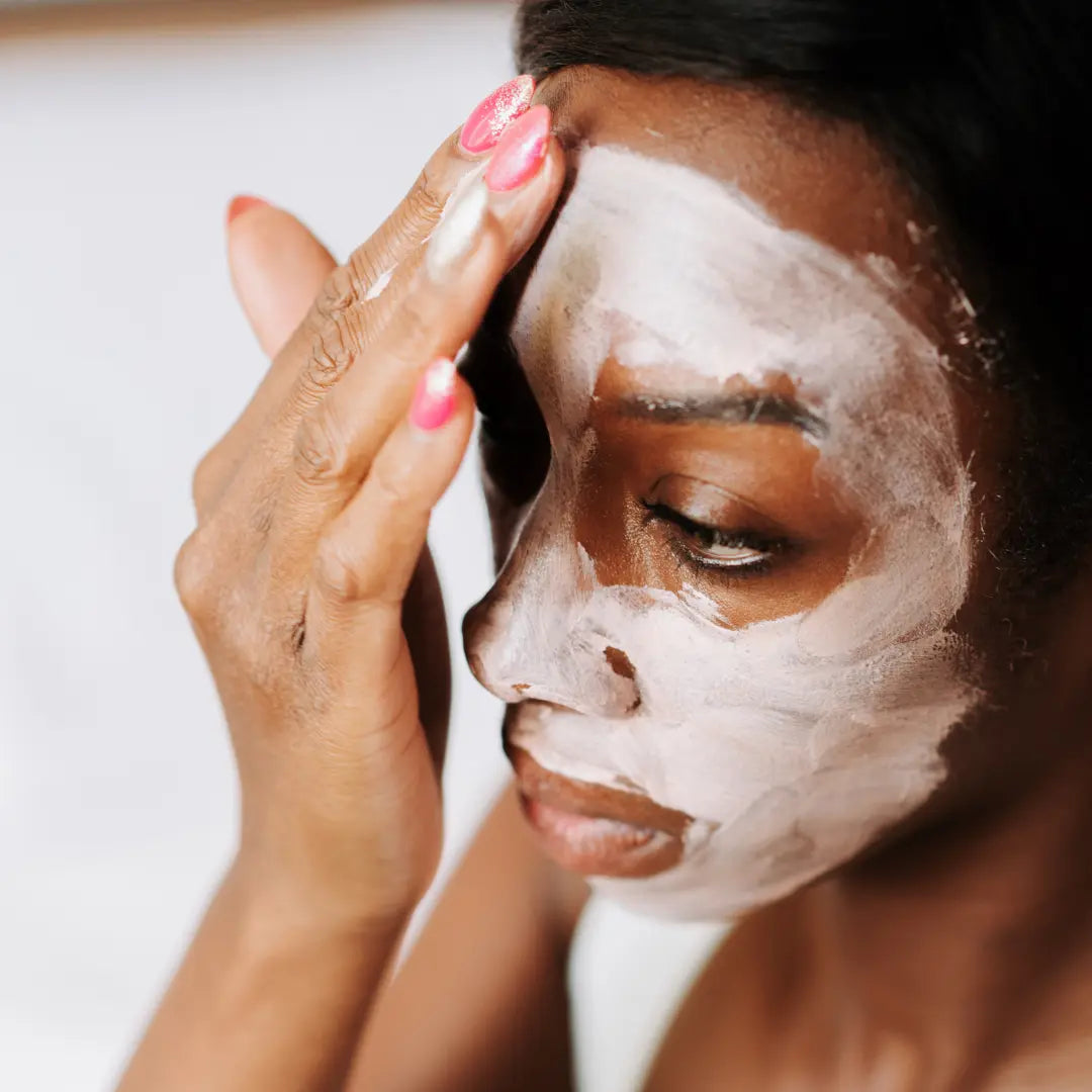 Une femme noire applique un masque à l'argile sur le visage.