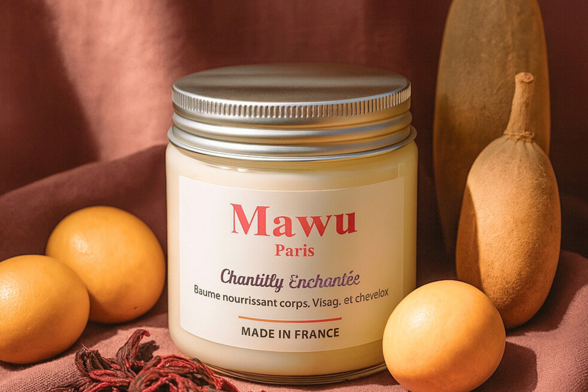 Baume nourrissant au karité Chantilly Enchantée entouré de fruits marula et de feuilles d'hibiscus.